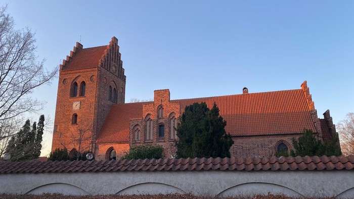 Røde murstenskirke med spire og arkadefænstre.