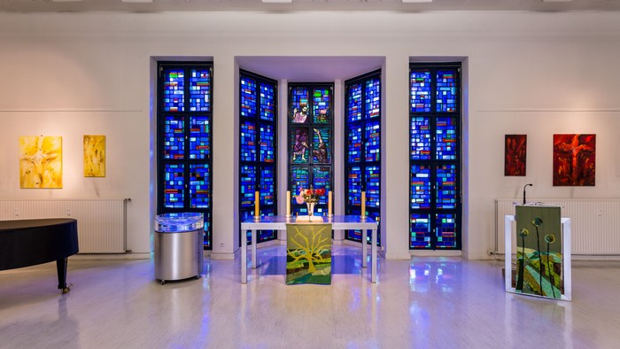 Moderne Kapelle mit Innenraumgestaltung durch Buntglasfenster, abstrakter Kunst und minimalistischem Altar-Design.