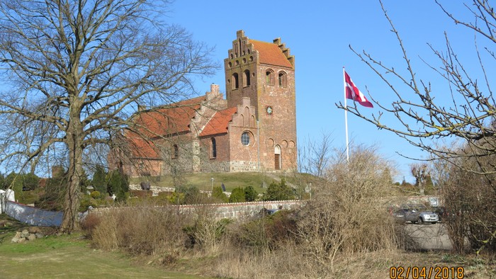 En gammel kirke med tårn og røde tag, flag på en stang ved siden af.