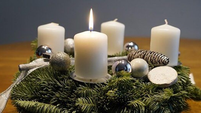 Adventskranz mit weißen Kerzen. Eine der Kerzen brennt.