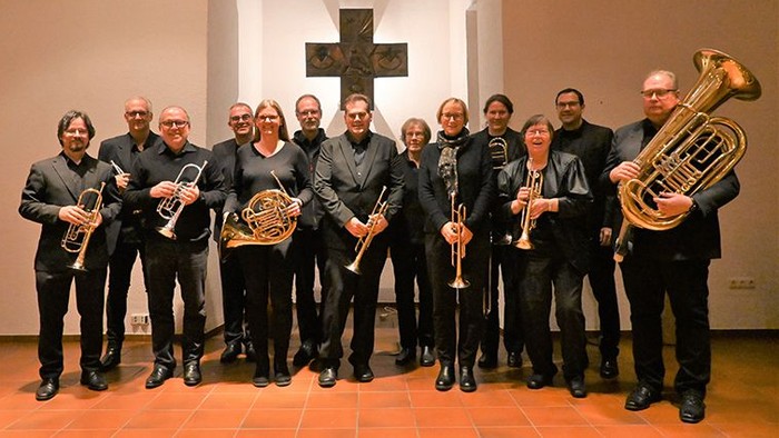 Eine Gruppe aus Bläserinnen und Bläsern vor einem kunstvoll gestalteten Kreuz in einer Kirche