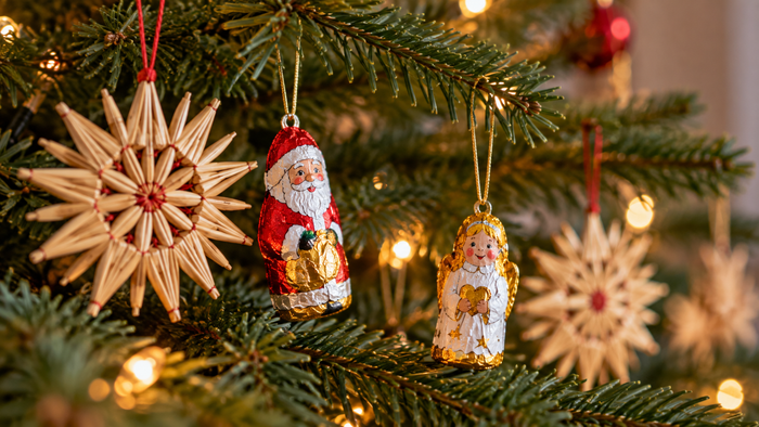 Tannenzweige eines festlich beleuchteten Weihnachtsbaums sind mit Strohsternen sowie kleinen Schokofiguren von Weihnachtsmann und Engel geschmückt.