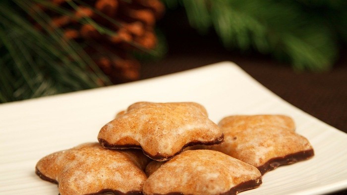 Weihnachtliche Plätzchen auf weißem Teller mit Tannenzapfen und Beeren im Hintergrund