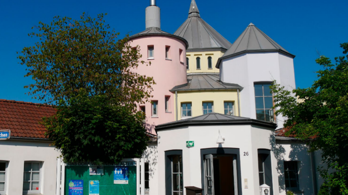 Buntes historisches Gebäude mit runden Türmen und einem markanten Baustil, umgeben von Grünflächen.