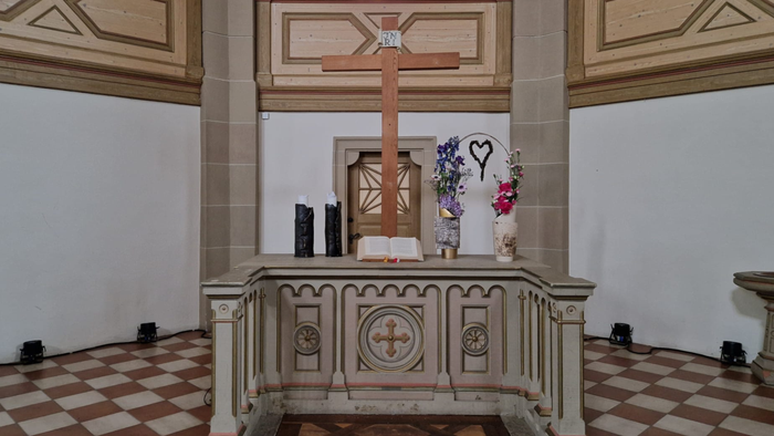 Das Bild zeigt einen Altar in einer Kirche mit Kreuz, Kerzen und Blumen.