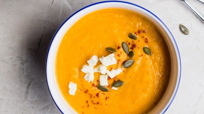 To skåler med pumpesuppe og pumpefrø, spiseløg og skøb.
