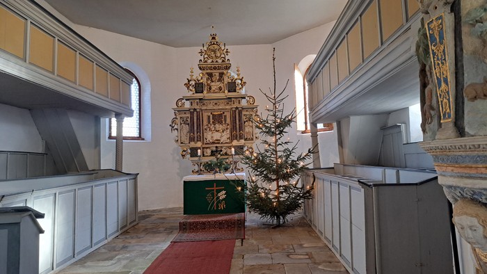 In der Kirche steht ein geschmückter Weihnachtsbaum vor einem Altar.
