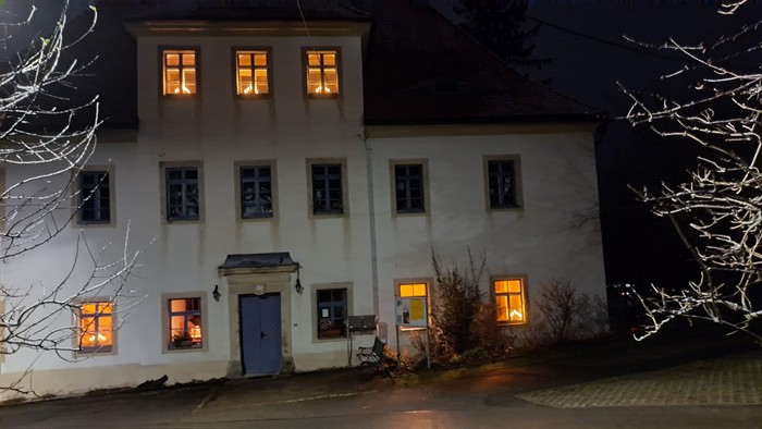 Ein altes, weißes Haus mit warmen Lichtern in den Fenstern bei Nacht.