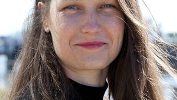 Eine Frau mit langen braunen Haaren lächelt in die Kamera.