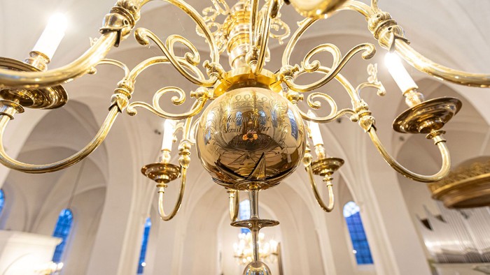 Eleganter goldener Kronleuchter mit aufwendigen Verzierungen, der in einem großen, gewölbten Innenraum hängt.