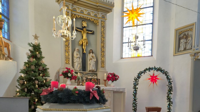 Elegante Kircheninnenausstattung mit festlichen Dekorationen, darunter ein Taufbecken, ein Altar und Weihnachtsbäume.