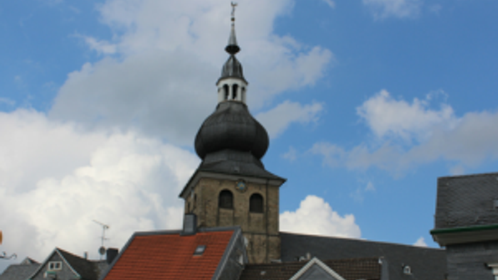 Ein Kirchturm mit schwarzer Kuppel und Kreuz steht vor blauem Himmel mit Wolken.