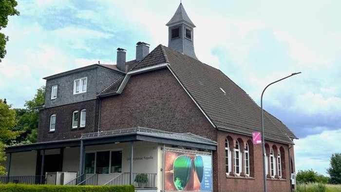 Eine malerische Backsteinkirche mit einem kleinen Turm und einem bunten Wandgemälde an der Außenwand neben einer Straße.