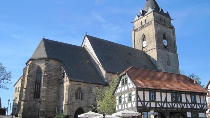 Außenansicht der Evangelischen Stadtkirche Wolfhagen. Großes Natursteingebäude mit hohem Turm und dunklem Schieferdach.