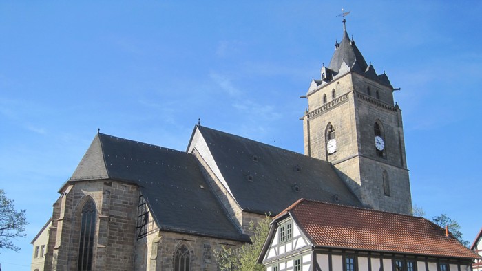Außenansicht der Evangelischen Stadtkirche Wolfhagen. Großes Natursteingebäude mit hohem Turm und dunklem Schieferdach.