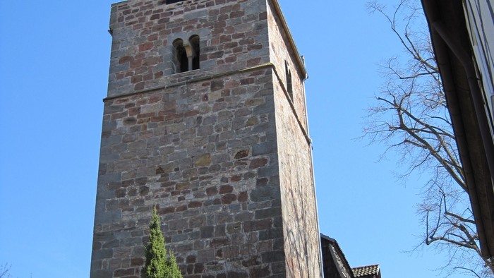 Außenansicht der evangelischen Kirche in Niederelsungen mit hohem Natursteinturm, gestufter Giebelzone und spitzer Dachhaube. 