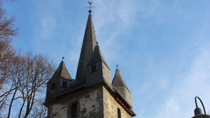 Außenansicht der evangelischen Kirche in Altenhasungen. Hoher Natursteinturm mit mehreren spitzen Schieferhauben.