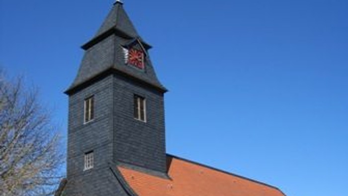 Außenansicht der evangelischen Kirche in Bründersen von Südwesten. Natursteingebäude mit rotem Ziegeldach und dunklem Turm.