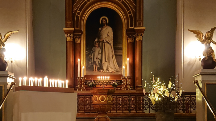 Elegant kirkealter med en statue af Jesus, tændte lys og prægtige gyldne dekorationer med englefigurer.