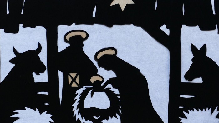 Schwarze Silhouetten von Maria, Josef und Baby Jesus in der Krippe, umgeben von Tieren und einem Sternenhimmel