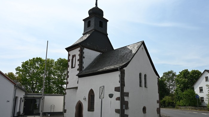 Idyllische weiße Kirche mit dunklem Kirchturm und gewölbtem Eingang in einer Kleinstadt.