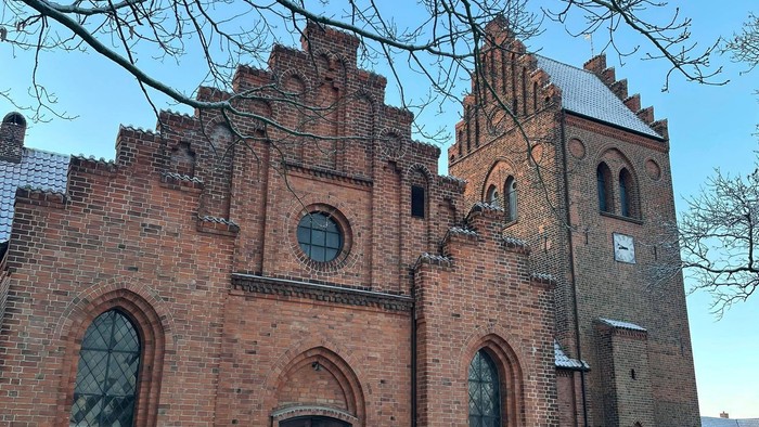 Gamle teglsteinskirke med spisse tårne og buevinduer.