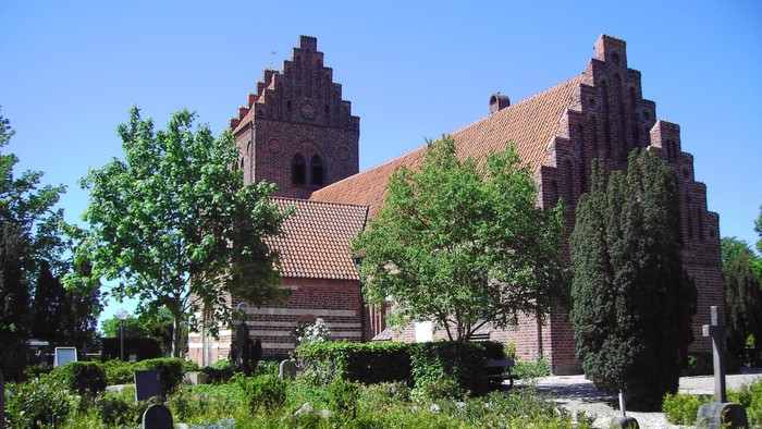 En stor murstenskirke med spisse tårne og omgivet af grønne træer og en græsplæne