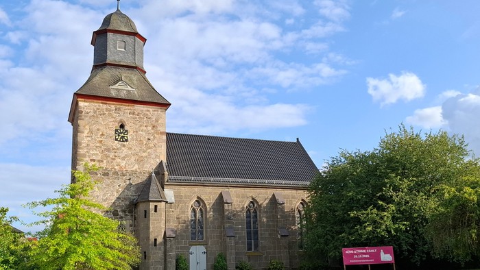 Historische Steinkirche mit hohem Glockenturm in einer üppigen, grünen Landschaft.