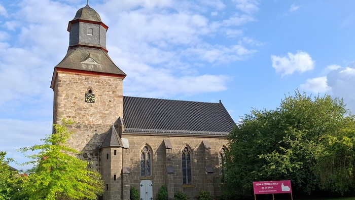 Historische Steinkirche mit hohem Glockenturm in einer üppigen, grünen Landschaft.