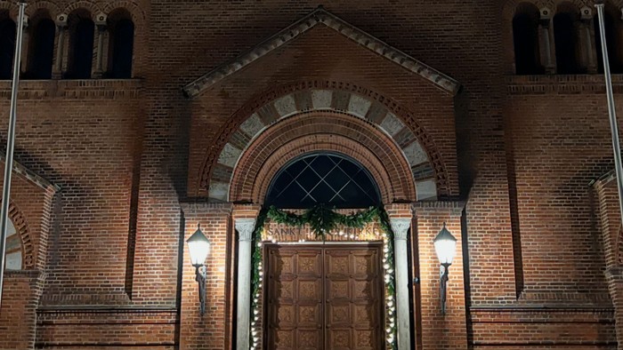 Elegant murstenskirkefacade pyntet med festlige lys og en stor buet indgang om natten.