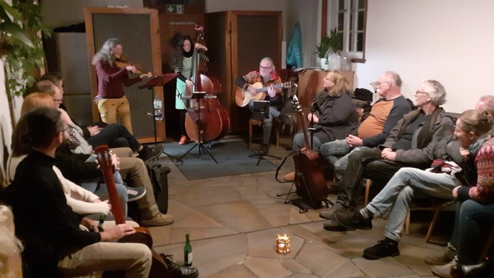 Eine gemütliche Indoor-Veranstaltung mit Musikern, die für ein aufmerksames Publikum in einem warm beleuchteten Raum auftreten.