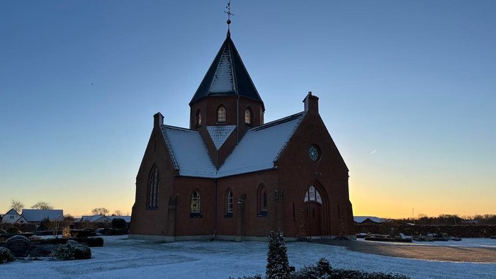 Sneklædt kirke med tårn og bjerge i baggrunden ved solnedgang.