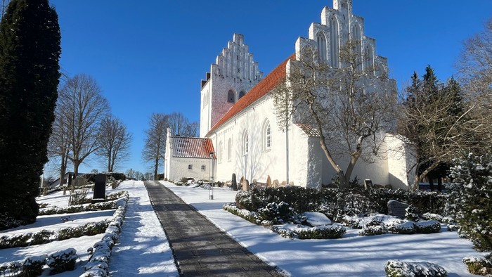 Kirke med høje spir, omgivet af sneklædt landskab.