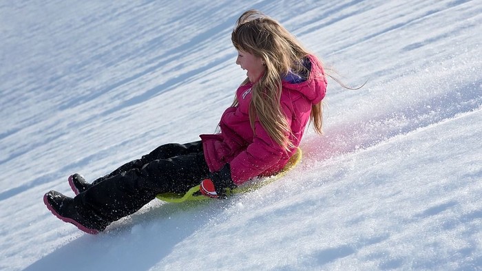 Et barn slemmer på sne med en sled.