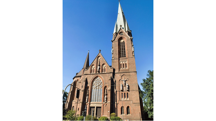 Große Backsteinkirche mit hohem Turmspitz und Rundbogenfenstern.