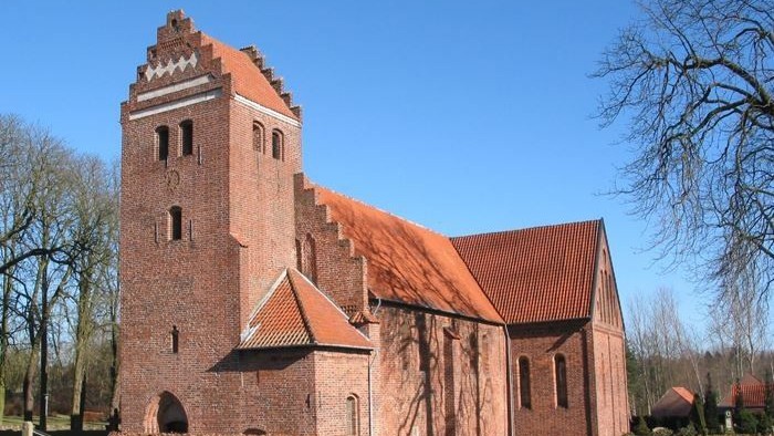 Røde murstenskirke med tårn og spids tag.
