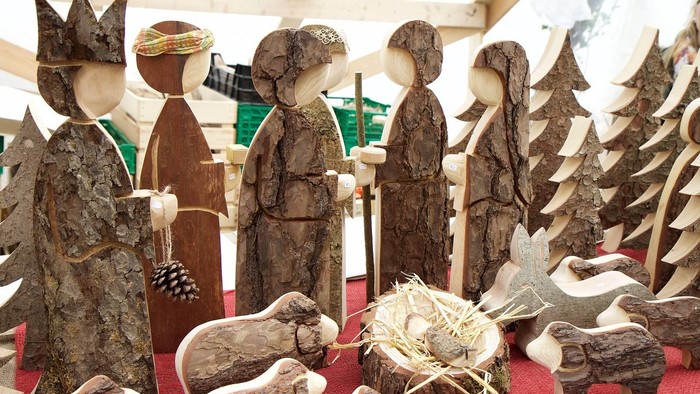 Künstlerisch arrangierte, handgeschnitzte Holzfiguren und Tiere einer Weihnachtskrippe auf einer roten Auslage.