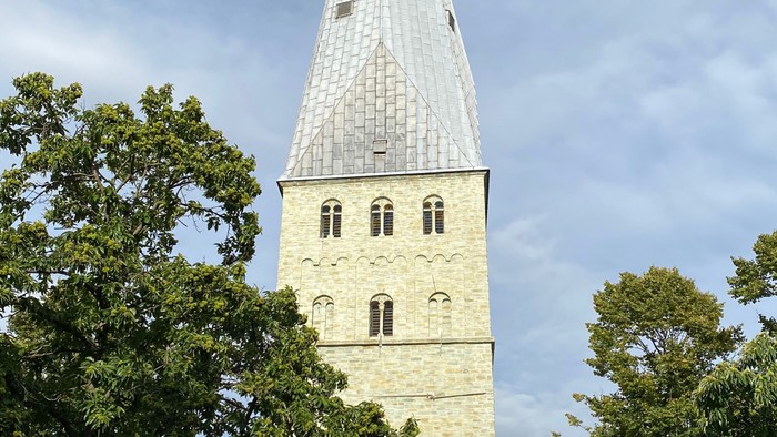 Hohe Kirche mit spitzem Turm und Uhr, umgeben von Bäumen