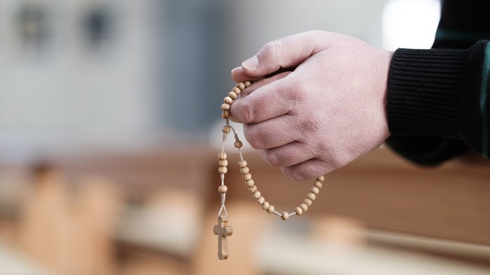 Eine Hand hält ein Rosenkranz mit Kreuz in einer Kirche.