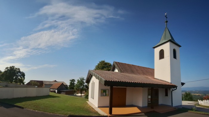 Kleine weiße Kirche mit grünem Turm auf grasbewachsenem Hügel unter blauem Himmel