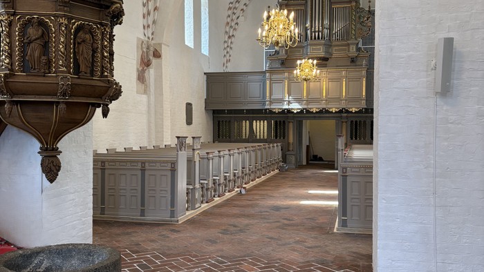 Indgang til en stor kirke med høje vægge og orgel.