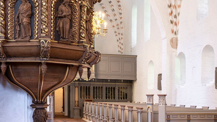 Indre del af kirke med altertavle og bænke.