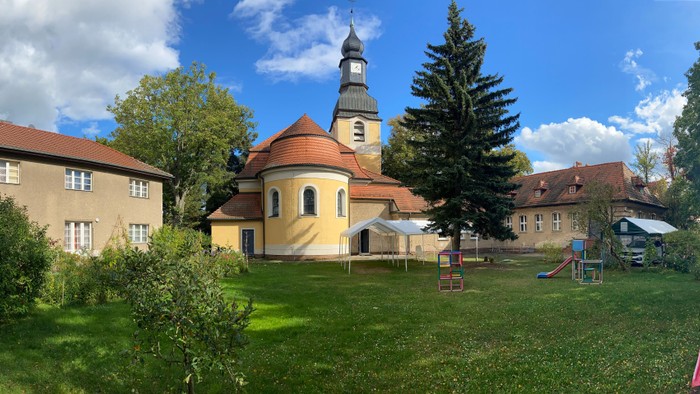 Ein Spielplatz neben einem gelben Gebäude mit Kirche und grünem Gras