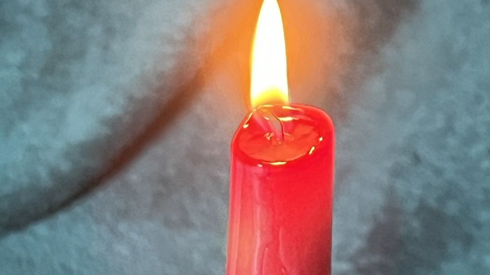 Eine rote Kerze brennt vor einem blauen Hintergrund.