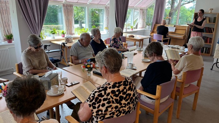 En gruppe ældre mennesker samlet omkring borde i et veloplyst rum, optaget af forskellige aktiviteter.