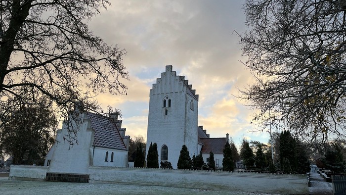 En snedækket park med en centralt beliggende hvid kirke med tårn og et mindre sidebygning.