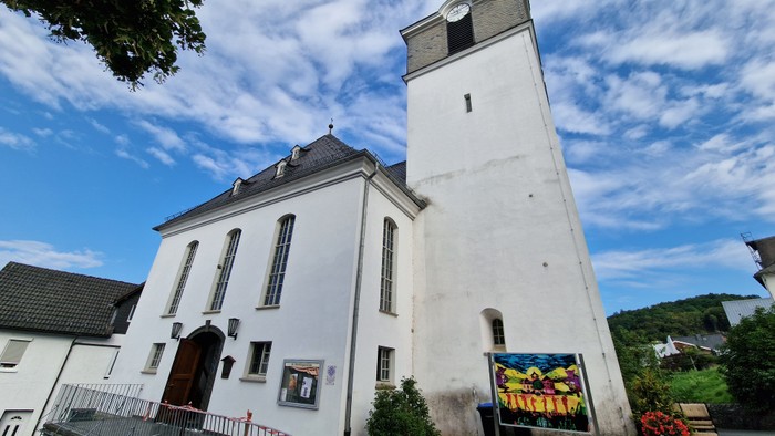 Weißes Kirchengebäude mit hohem Turm und Uhr unter blauem Himmel