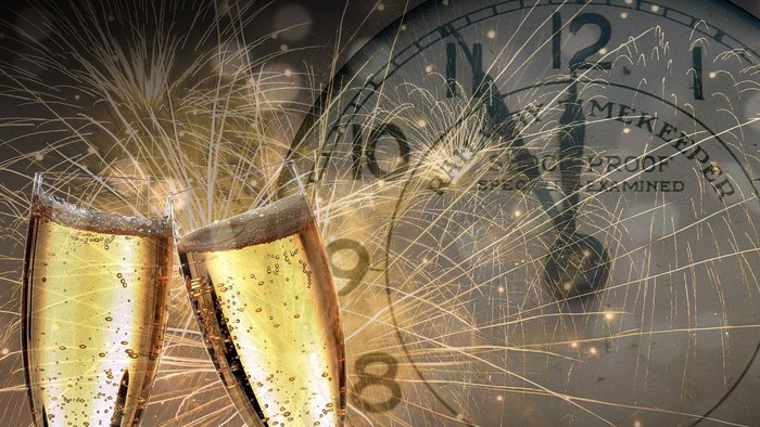 Zwei Champagnergläser stoßen auf Silvesterfeuerwerk vor Uhr.