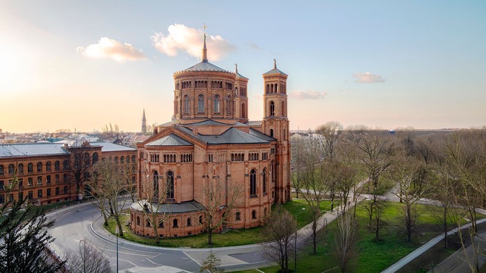 Imposante Backsteinkathedrale, umgeben von üppigem Grün und weitläufigen Campusgeländen unter klarem Himmel.