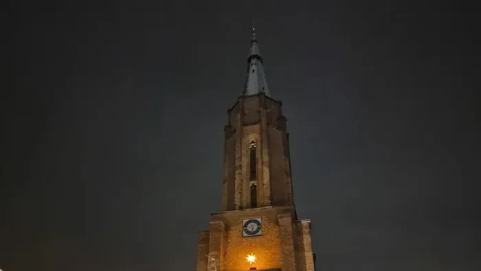 Ein beleuchteter Kirchturm bei Nacht mit Uhr und Weihnachtslichtern